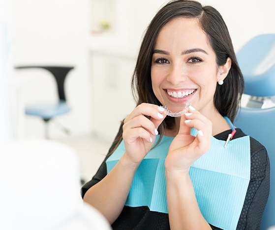 Smiling woman in dental chair holding at Nu Smile Aligner tray