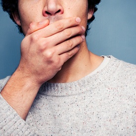 Man in gray sweater covering mouth, embarrassed by his crossbite