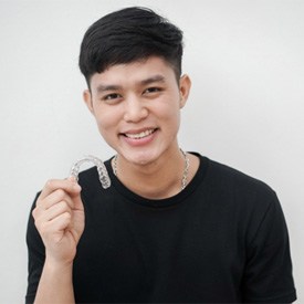 Smiling young man holding Invisalign alternative in Brick  