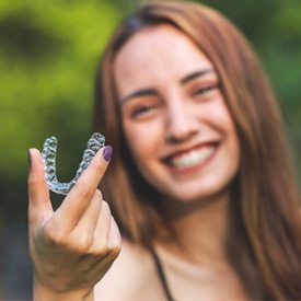 woman smiling while holding clear aligner
