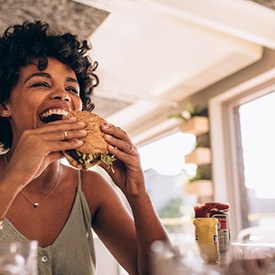 Woman smiling while eating a burger at restaurant