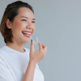 Woman in white shirt smiling while holding Invisalign aligner