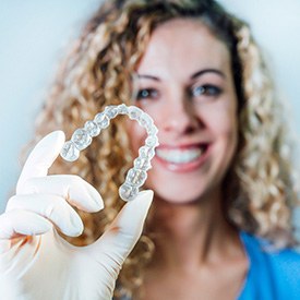 Smiling dental assistant holding Invisalign aligner out in front of her