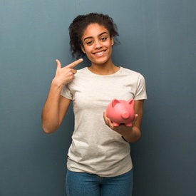 woman holding pink piggy bank and pointing to her smile