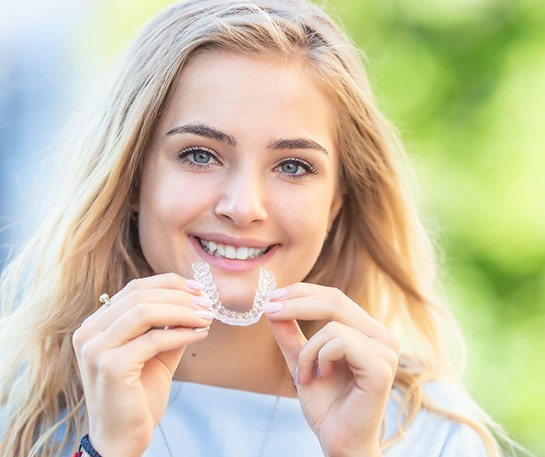 Smiling teen girl with blond hair holding Nu Smile aligner