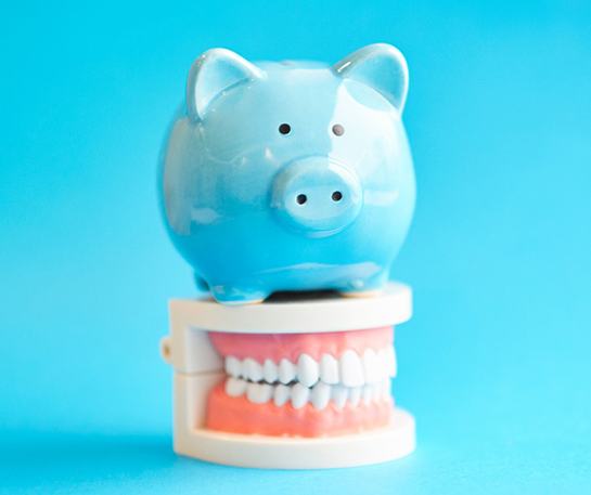 Piggy bank atop model teeth representing cost of Invisalign in Brick 