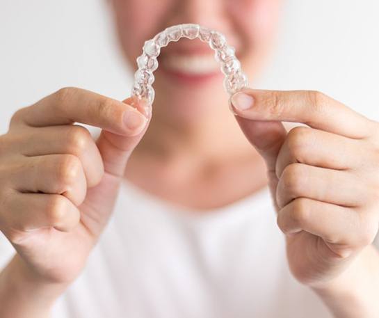 Smiling woman holding up Invisalign in Brick 