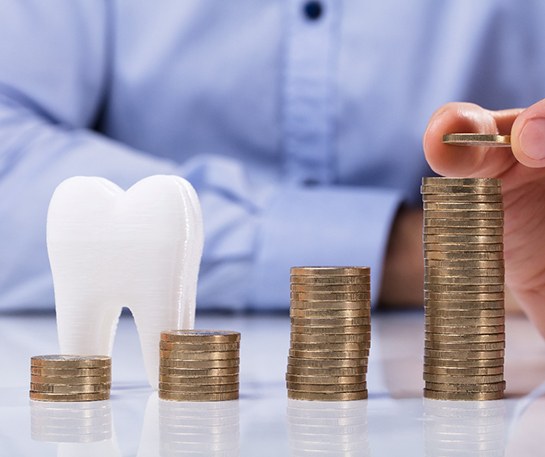 model tooth and coin stacks representing cost of Invisalign in Staten Island 