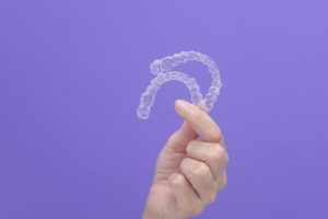 Hand holding two clear aligners against purple background