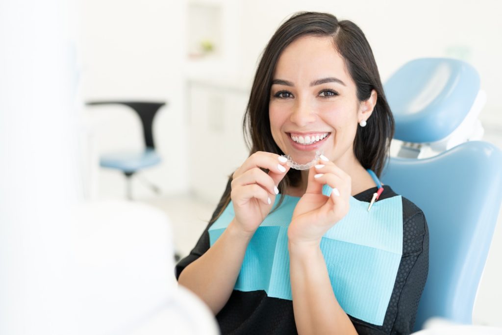 Woman smiling while holding NU Smile Aligner in treatment chair