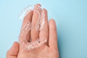 Clear aligners resting on the palm of a hand over a blue background