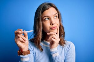 Woman holding clear aligner, wearing curious expression